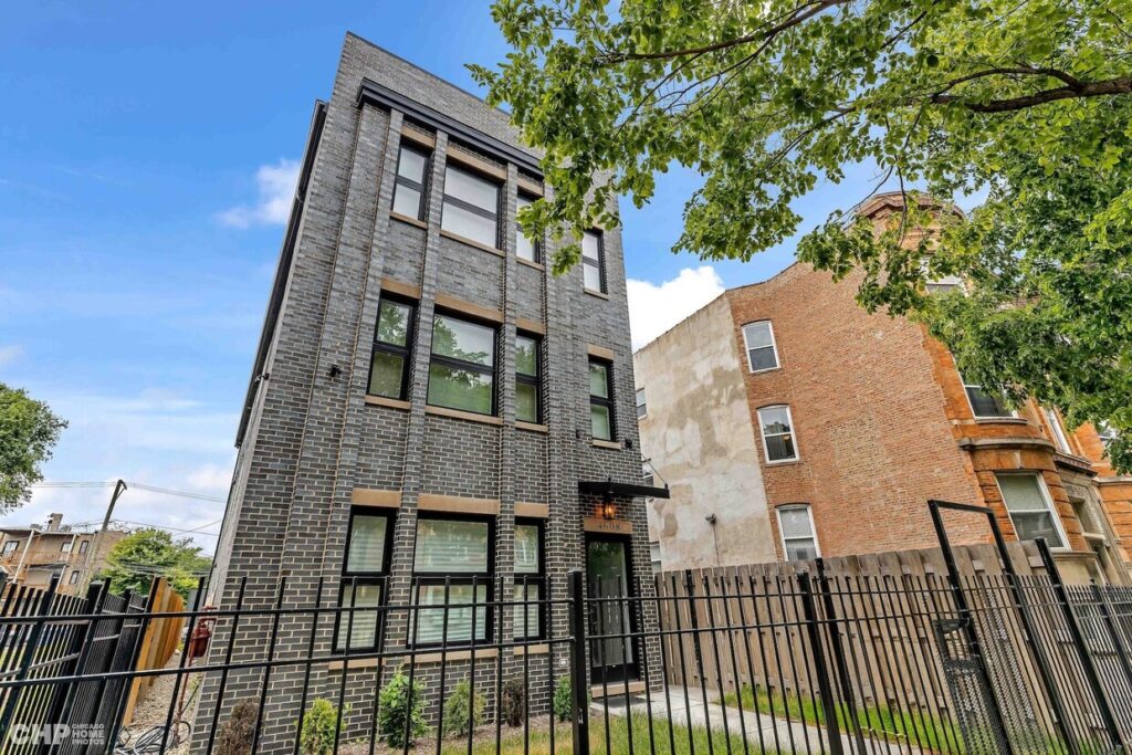 Two apartments buildings surrounded with a black fence along with beautiful cloudy sky and trees