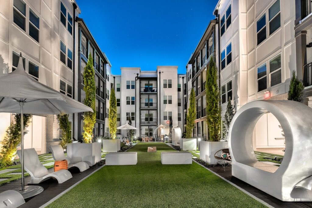 a courtyard in the middle of a large apartment building with a lawn and lounge chairs